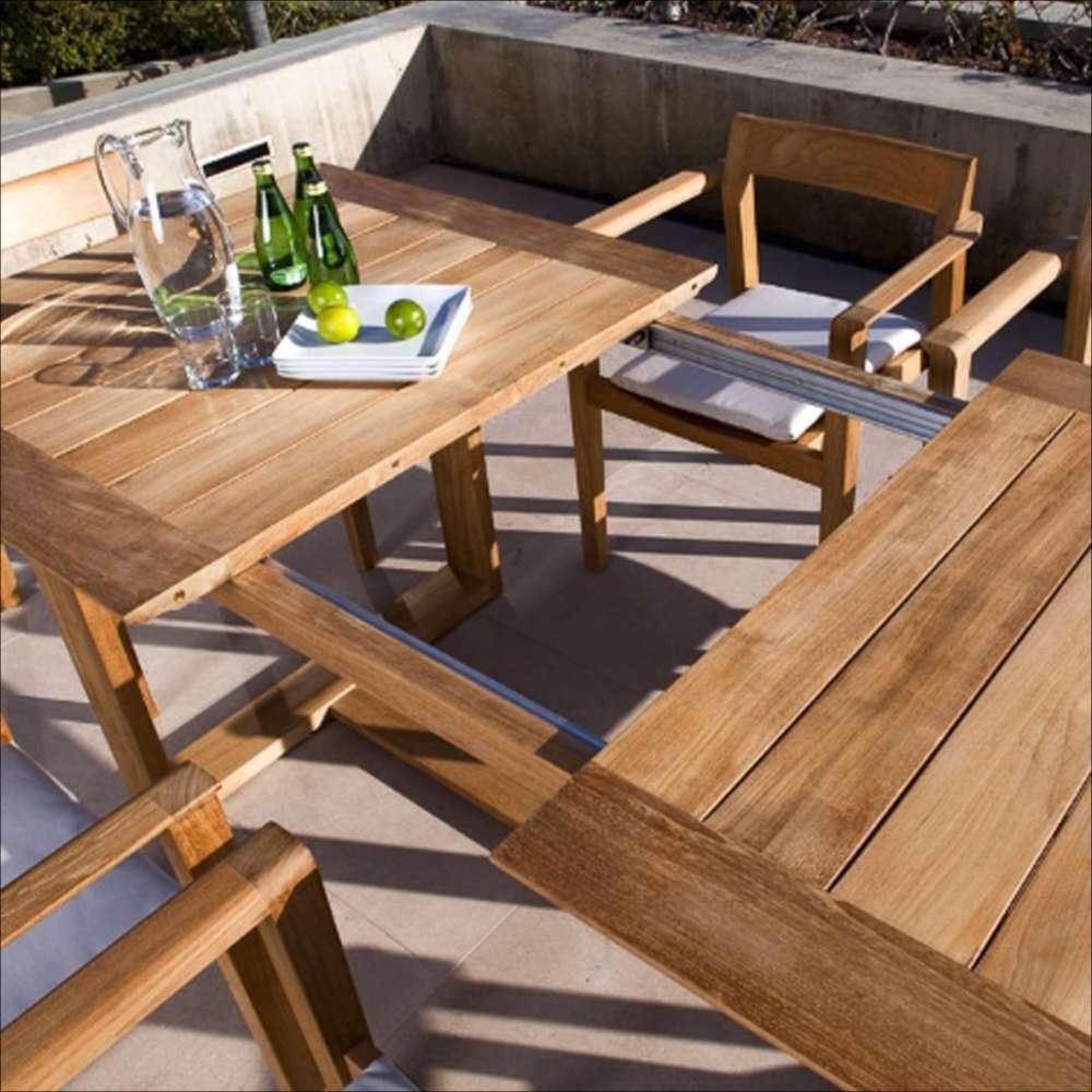 Westminster Teak Horizon 11pc Teak Dining Set with a close angled view of the teak table outdoors, topped with a glass pitcher, bottles, a plate, and limes