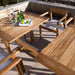 Westminster Teak Horizon 11pc Teak Dining Set with a close angled view of the teak table outdoors, topped with a glass pitcher, bottles, a plate, and limes