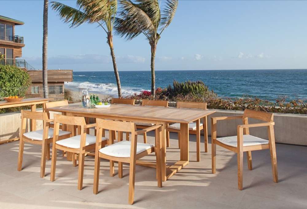 Westminster Teak Horizon 9pcs Teak Dining Set placed on an outdoor balcony by the ocean, with cushioned chairs around a teak table holding drinks and limes