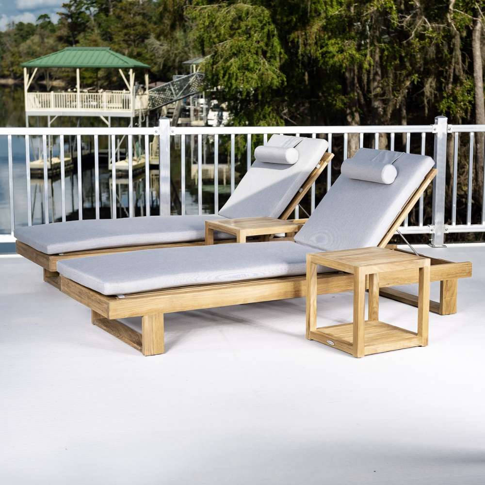 Westminster Teak Horizon Double Chaise and Side Table Set placed on a patio overlooking a dock and trees, featuring two cushioned loungers and matching side tables