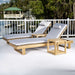 Westminster Teak Horizon Double Chaise and Side Table Set placed on a patio overlooking a dock and trees, featuring two cushioned loungers and matching side tables
