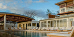 Westminster Teak Horizon Double Chaise and Side Table Set shown in a resort setting with many similar loungers lined up beside a large swimming pool