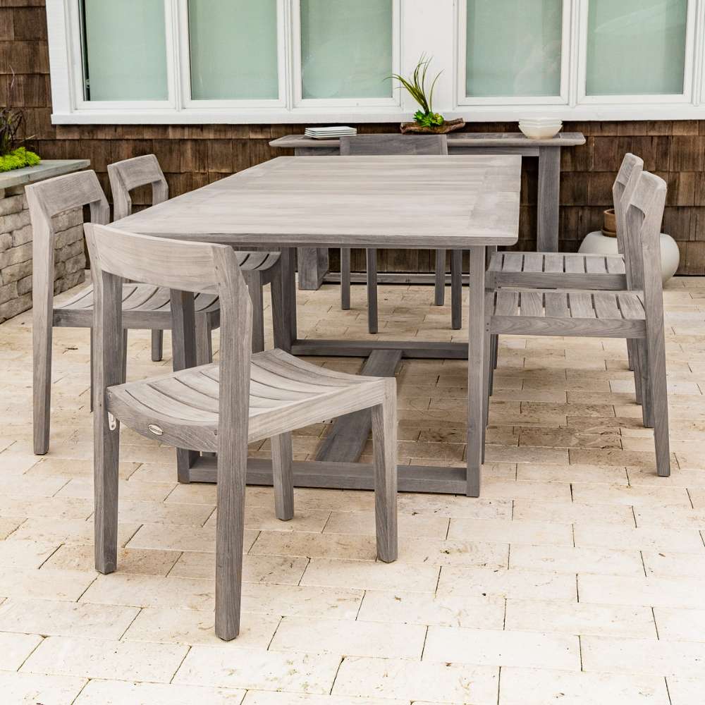 Westminster Teak Horizon Sidechair Dining Set for 6 shows the full outdoor dining set in a weathered gray teak finish placed on a stone patio beside a house