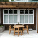 Westminster Teak Horizon Sidechair Dining Set for 6 shows the outdoor teak dining set from farther back under a wooden pergola, centered in front of a house