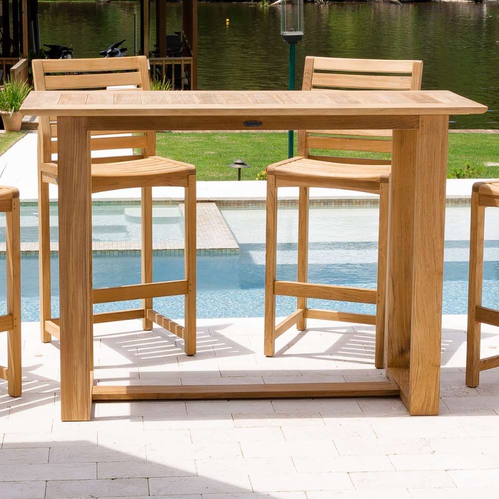 Westminster Teak Horizon Teak Bar Table is placed outdoors by a pool, paired with tall wooden bar stools on a light stone patio