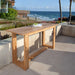 Westminster Teak Horizon Teak Console Table sits on a sunny patio with coastal views, displaying a natural wood finish and minimalist structure
