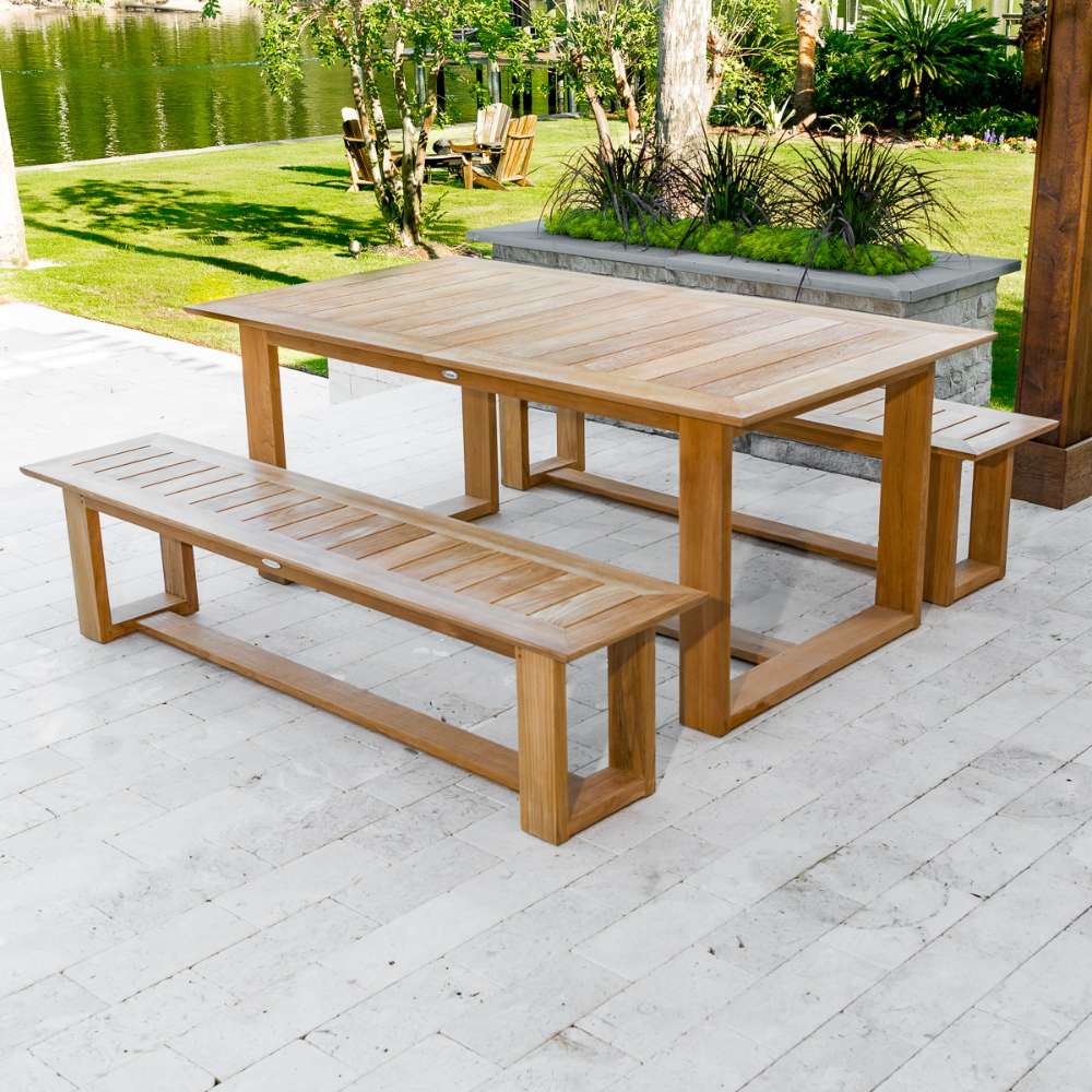 Westminster Teak Horizon Teak Dining Picnic Set on an outdoor patio with greenery, shrubs, and a scenic lake backdrop