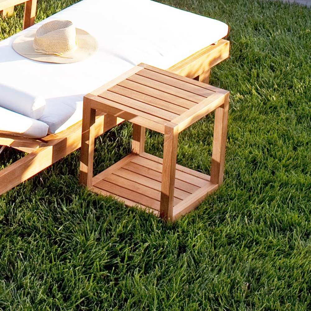 Westminster Teak Horizon Teak Side Table is placed on grass next to a lounge chair, showing its compact size and slatted design in a sunny outdoor setting