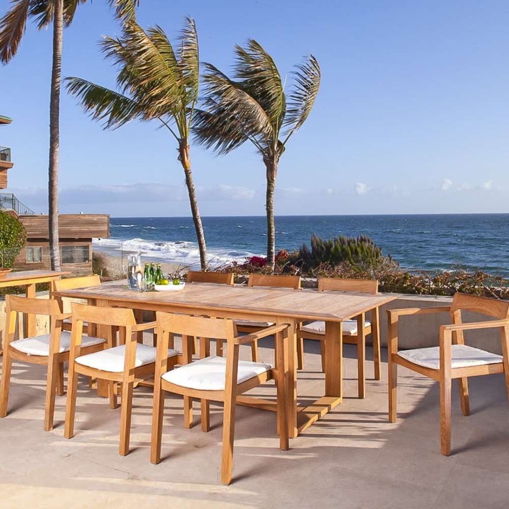 Westminster Teak Horizon Teak Table is set outdoors with matching chairs on a patio overlooking the ocean