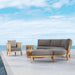 Westminster Teak Kafelonia 6pc Sofa Sectional Set with gray cushions, lounge chair, and tables on a patio overlooking the ocean