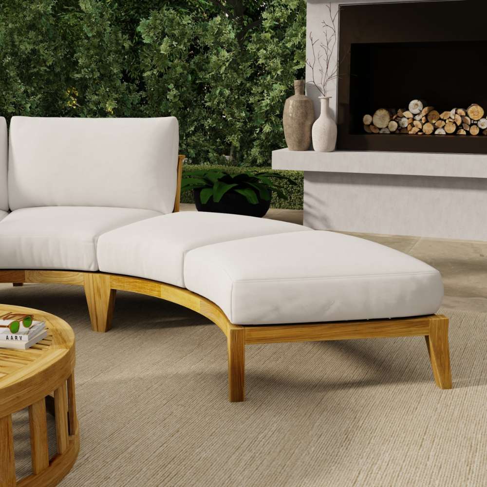 Westminster Teak Kafelonia Backless Sofa Sectional with white cushions curves beside a fireplace and greenery for a cozy outdoor lounge