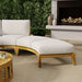 Westminster Teak Kafelonia Backless Sofa Sectional with white cushions curves beside a fireplace and greenery for a cozy outdoor lounge