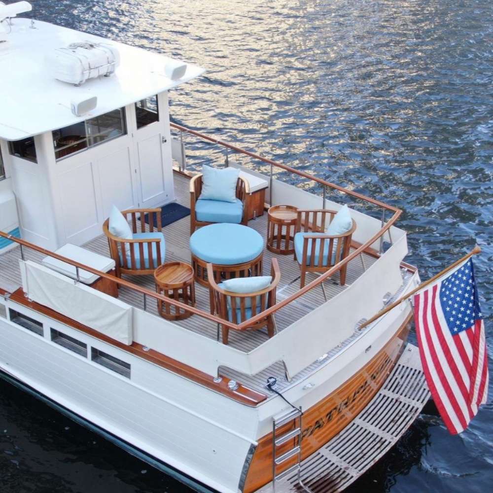 Westminster Teak Kafelonia Club Chair as part of a teak lounge set on a boat deck with blue cushions and ocean surroundings