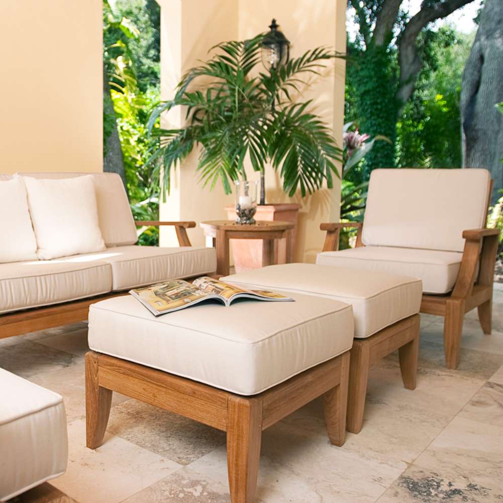 Westminster Teak Laguna Ottoman placed on an outdoor patio with matching cushioned chairs, used as a footrest or table with a magazine on top