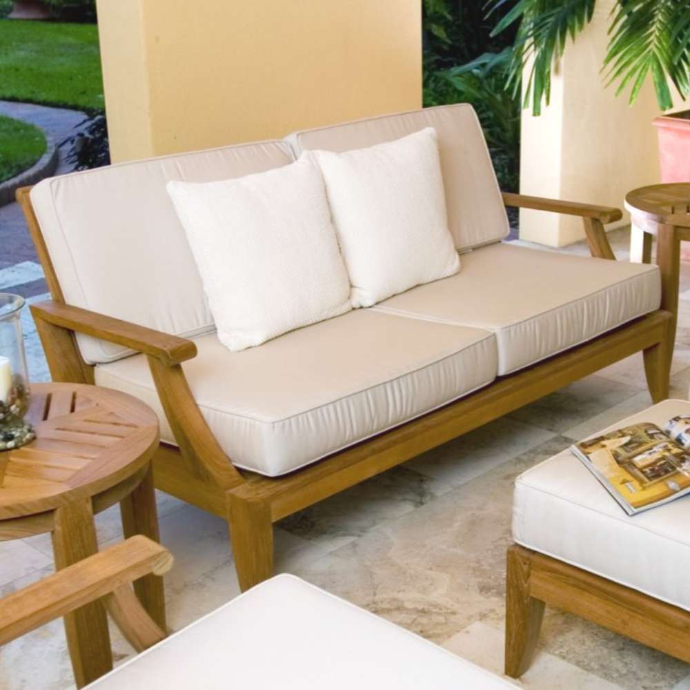 Westminster Teak Laguna Sofa appears in a cozy outdoor seating set with matching furniture, cushions, a small table, and surrounding greenery