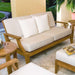 Westminster Teak Laguna Sofa appears in a cozy outdoor seating set with matching furniture, cushions, a small table, and surrounding greenery
