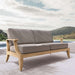 Westminster Teak Laguna Sofa sits outdoors on a patio with soft cushions, overlooking a pool and distant hills under a cloudy sky