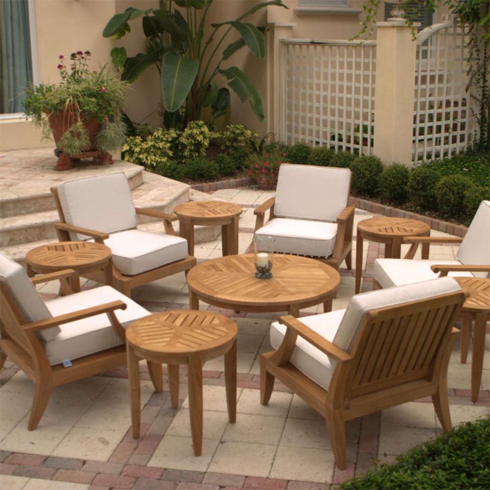 Westminster Teak Laguna Teak Lounge Chair is a part of a cozy outdoor patio set with several matching teak chairs, round tables, and cream cushions