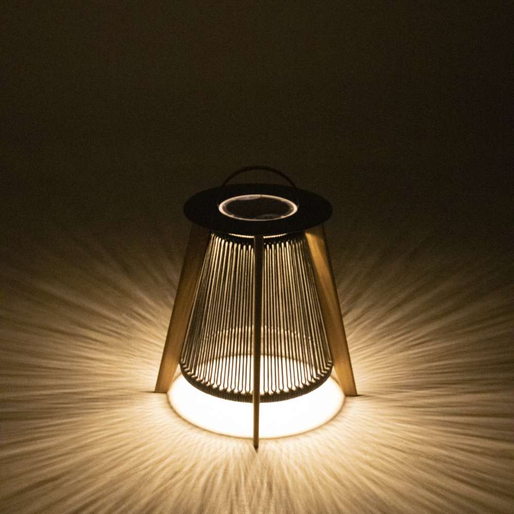 Westminster Teak Luna Large Lantern glows warmly in the dark, casting soft, radial light patterns through its vertical rope design onto the surrounding surface
