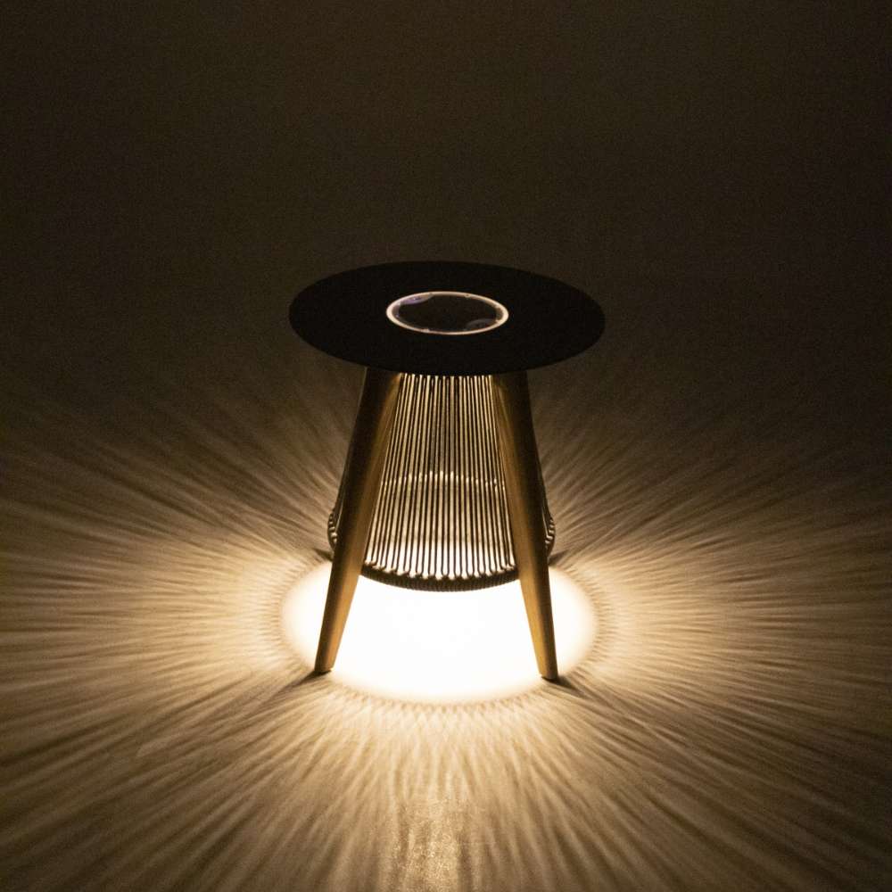 Westminster Teak Luna Round Side Table is displayed glowing in the dark, casting soft light patterns on the ground from its illuminated base