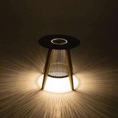 Westminster Teak Luna Round Side Table is displayed glowing in the dark, casting soft light patterns on the ground from its illuminated base