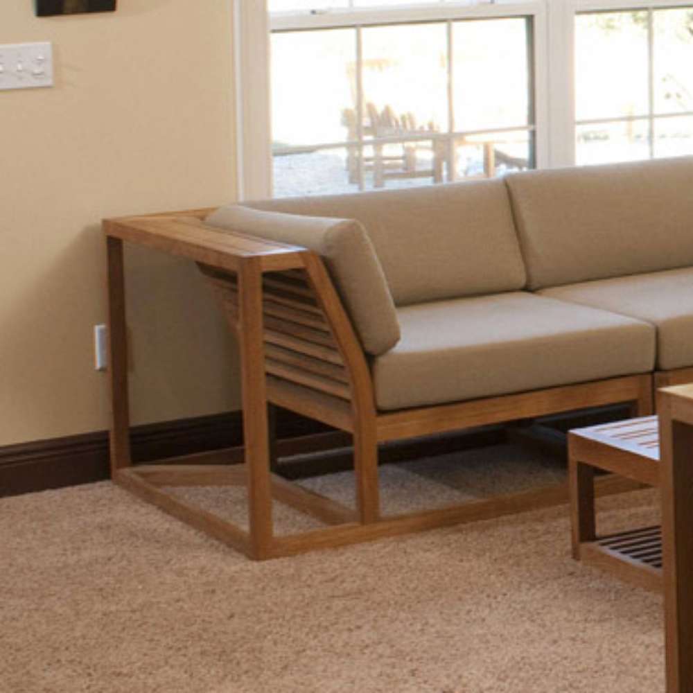 Westminster Teak Maya Corner Sectional appears indoors as a corner seat with a side table extension, showcasing its sturdy teak frame and neutral cushions in a cozy living space