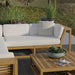 Westminster Teak Maya Left Side Sectional is displayed with soft cushions on a patio, surrounded by greenery, creating a relaxed outdoor seating area