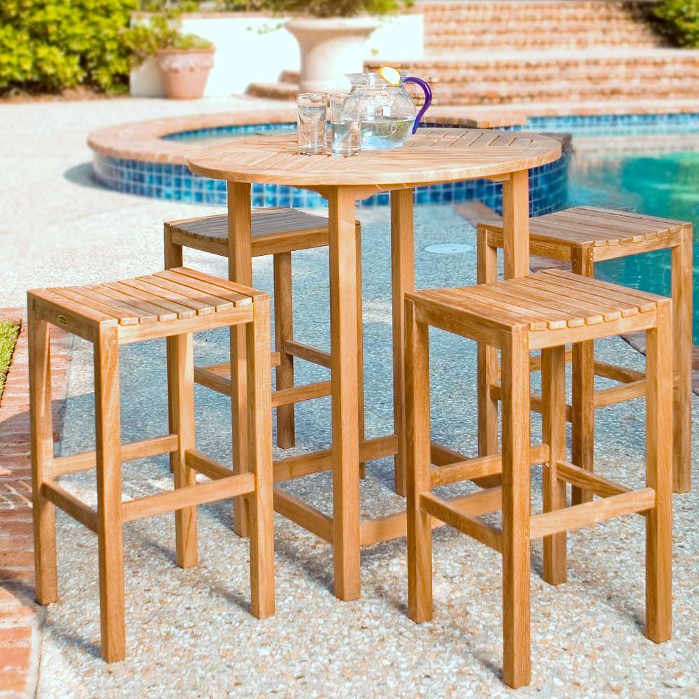 Westminster Teak Somerset Backless Bar Stool is arranged around a patio bar table holding a glass pitcher and cups near a pool and hot tub