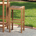 Westminster Teak Somerset Backless Bar Stool is placed outdoors on a patio beside another stool, with green grass in the background