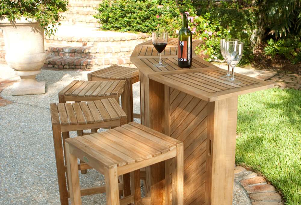 Westminster Teak Somerset Teak Bar angled patio setup with stools, drinks on top, and a landscaped garden background