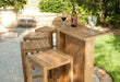 Westminster Teak Somerset Teak Bar angled patio setup with stools, drinks on top, and a landscaped garden background