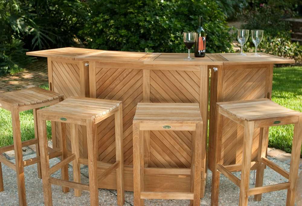 Westminster Teak Somerset Teak Bar outdoor patio setup with stools, wine glasses, and a bottle, surrounded by lush greenery