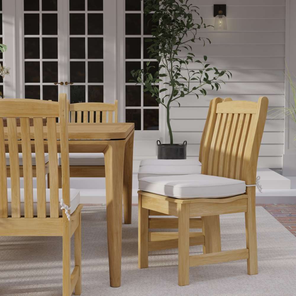 Westminster Teak Veranda Teak Dining Chair features a light cushion beside a teak table on a patio with white walls, French doors, and a potted plant