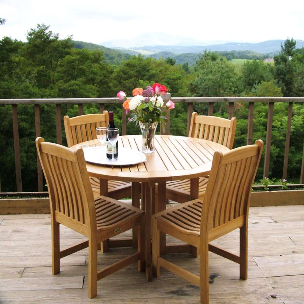 Westminster Teak Veranda Teak Dining Chair surrounds a round teak table on a deck with a mountain view, styled with flowers, wine, and glassware