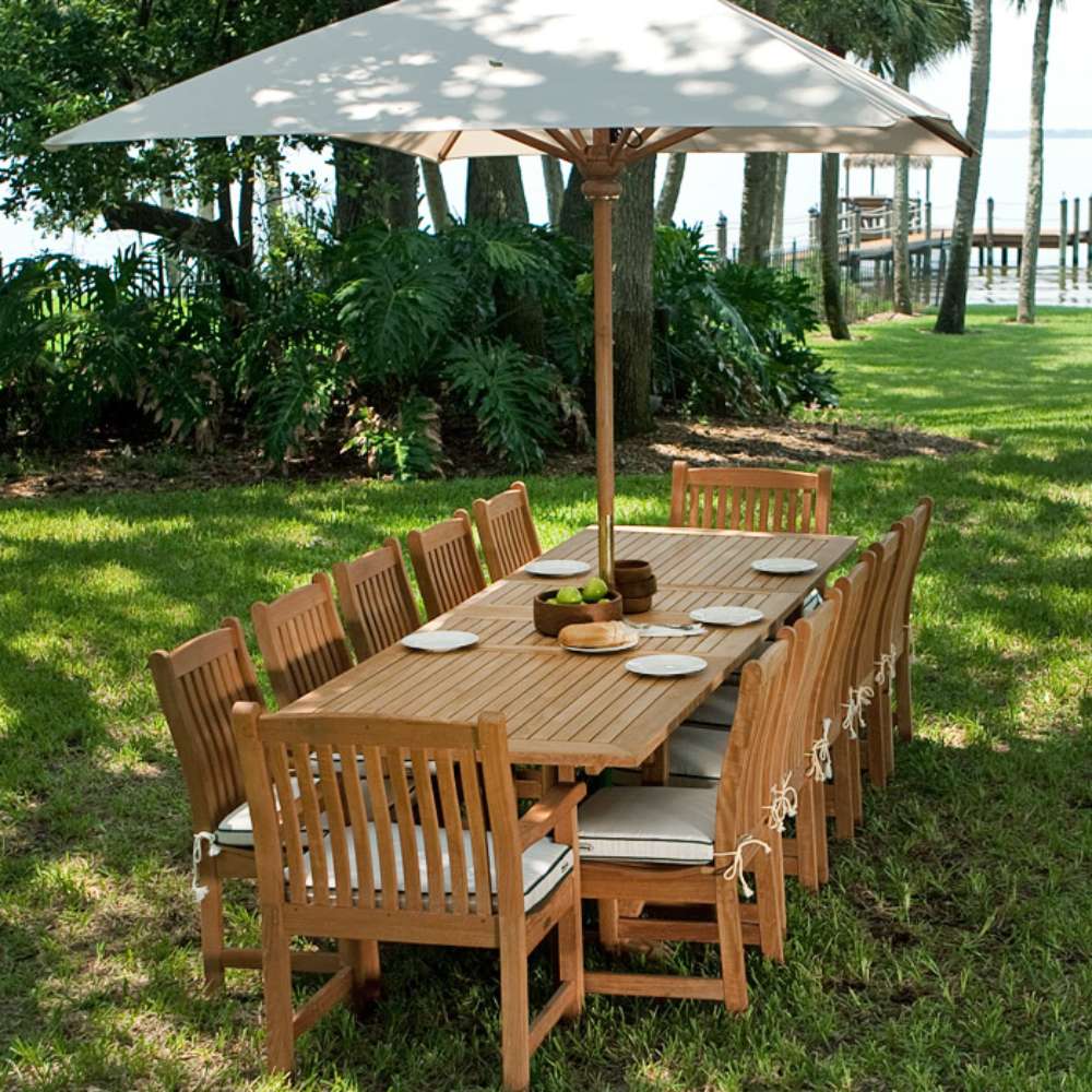 Westminster Teak Veranda Teak Table styled outdoors with matching teak chairs and a large umbrella on a grassy lawn by the water