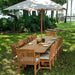 Westminster Teak Veranda Teak Table styled outdoors with matching teak chairs and a large umbrella on a grassy lawn by the water