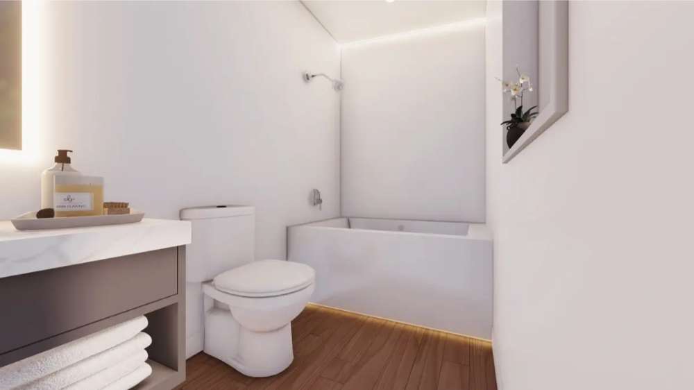 White bathroom in Sawmill Structures The Muskoka Garden Suites features a modern tub, toilet, vanity with towels, and soft under-cabinet lighting