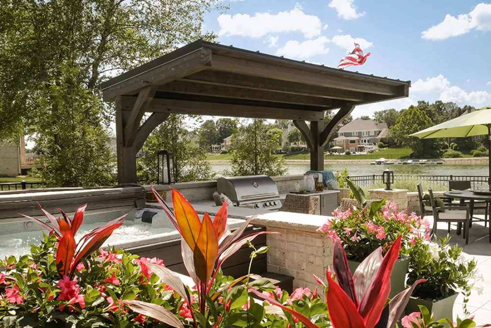 With vibrant flowers in the foreground, the Brookside Timber Frame Ledgefield Pavilion shelters an outdoor kitchen