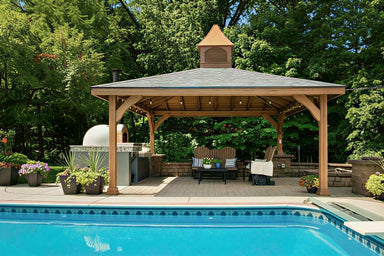 Wooden Brookside Timber Frame Forest Melody Pavilion covers a patio lounge with chairs and a table near a pool, with plants and forest greenery all around