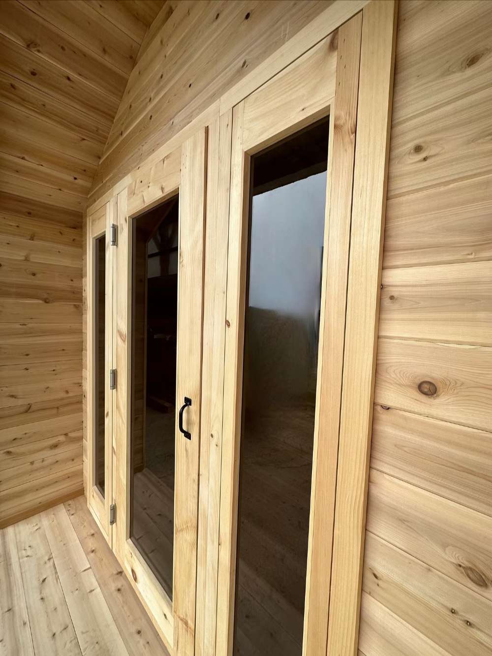 Wooden entrance of Sawmill Structures CabinSauna, with glass panels