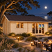 Light wood multi-room cabin with a gabled roof, glass doors, and windows illuminated at night near a beach fire pit.
