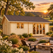 Rectangular light wood cabin with a gabled roof, glass doors, and windows at sunset near a stone fire pit.
