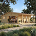 Exterior daytime view of the Bente 70 wooden cabin setup as a modern garden office, featuring a desk with shelving inside, a covered side porch with seating, and a stone walkway.