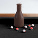 Black Crate & Barrel Walnut Pool Table with Wall Rack and Accessories in close up on a brown shake bottle standing on the black felt with small numbered red and white peas scattered around it