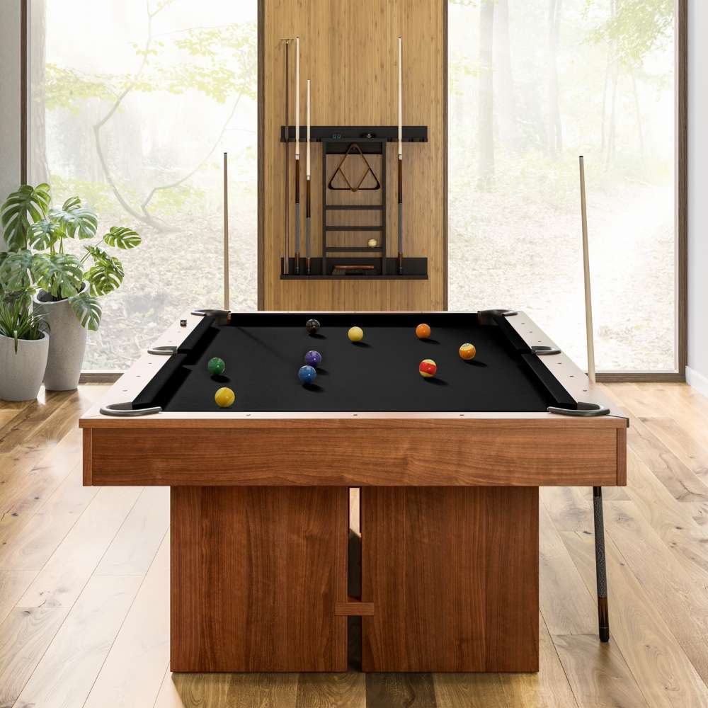 Black Crate & Barrel Walnut Pool Table with Wall Rack and Accessories seen end on in a room with floor to ceiling windows onto woodland, coloured balls on the black felt and a cue rack on the wall behind