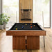 Black Crate & Barrel Walnut Pool Table with Wall Rack and Accessories seen end on in a room with floor to ceiling windows onto woodland, coloured balls on the black felt and a cue rack on the wall behind