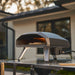 Black Ooni Koda 2 Pizza Oven on an outdoor kitchen counter at dusk with a pizza baking in the glowing mouth.