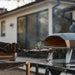 Black Ooni Koda 2 Pizza Oven with a gloved hand sliding a pizza peel toward the mouth outside a modern house.
