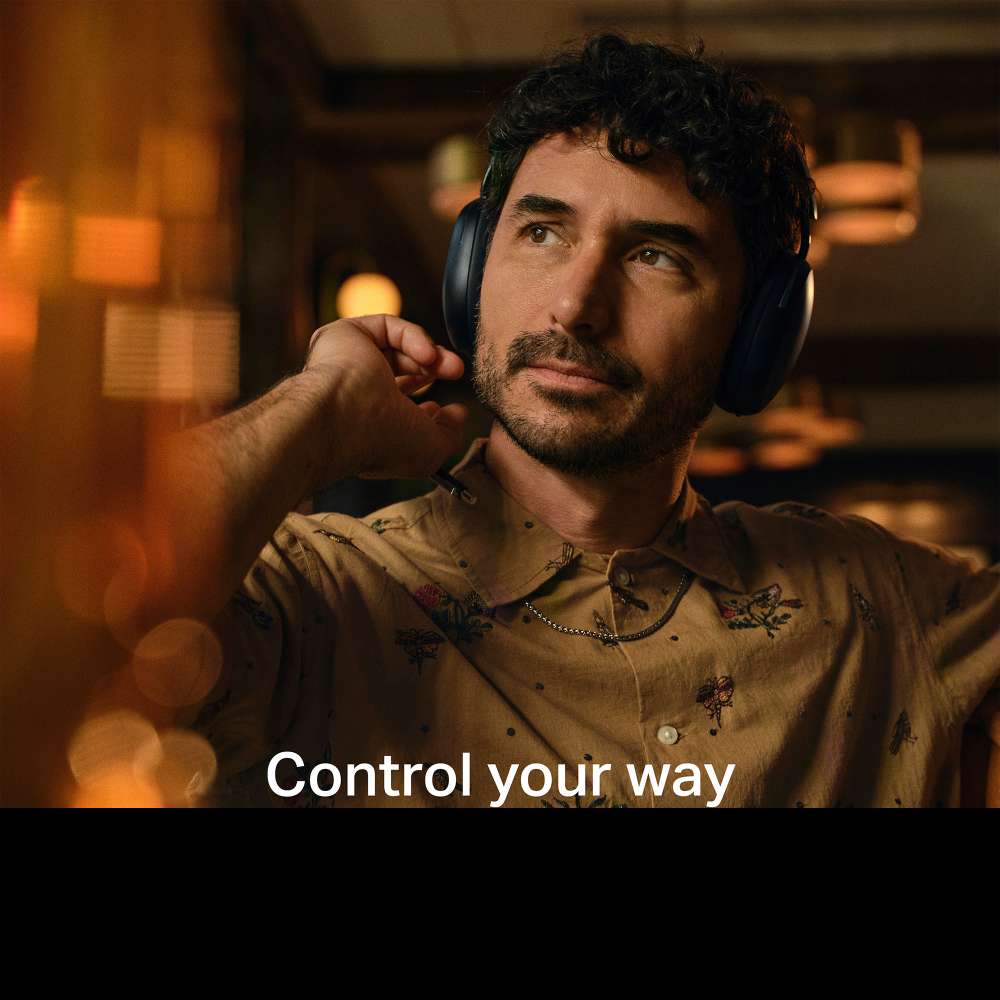 Black Sonos Ace Wireless Headphones with Noise Cancellation a man wearing the headphones and touching one earcup in a warmly lit bar with the words Control your way across the bottom