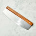 Crate & Barrel Rocker Pizza Cutter resting diagonally on a white marble countertop, the polished blade catching the light below the riveted wood handle.